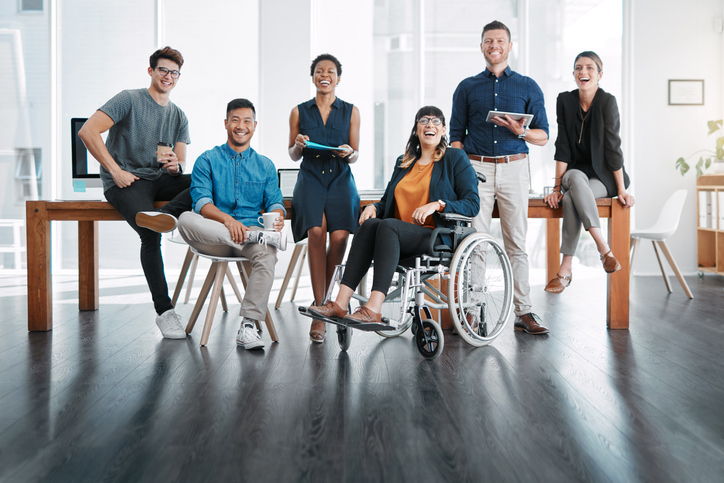 a group of six multi-ethnic business people in a bright office. One person is in a wheelchair.